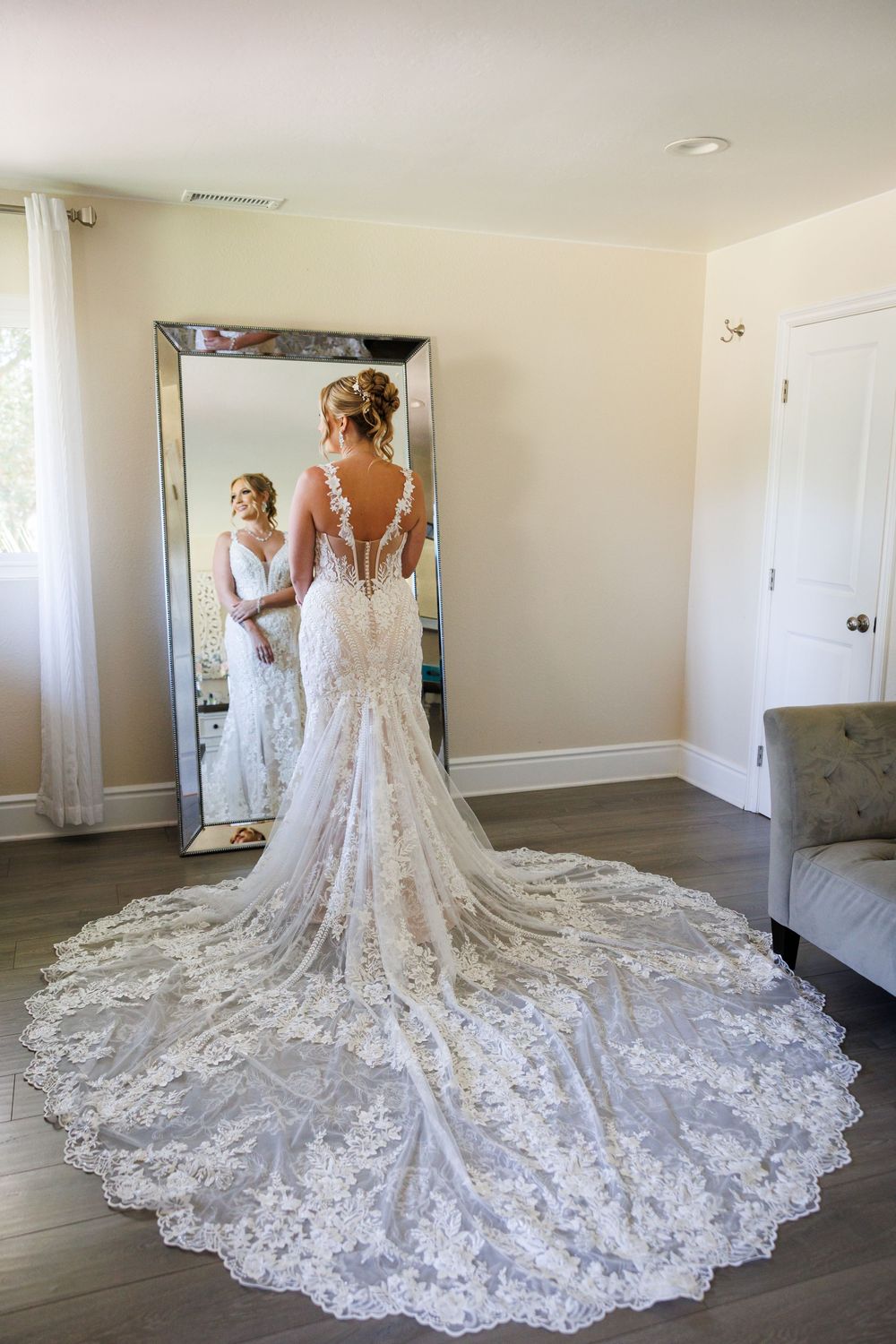 A stunning lace wedding gown with an elaborate cathedral-length train displayed from multiple angles in a room.