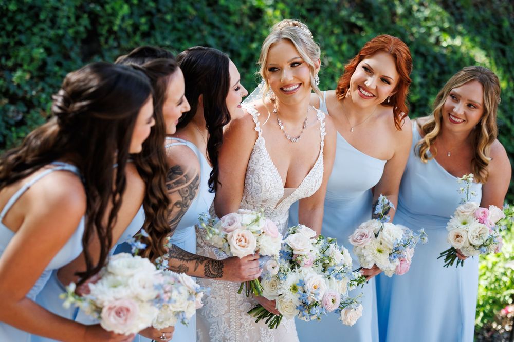 Bridesmaids in light blue dresses holding pink and white floral bouquets at an outdoor wedding ceremony.