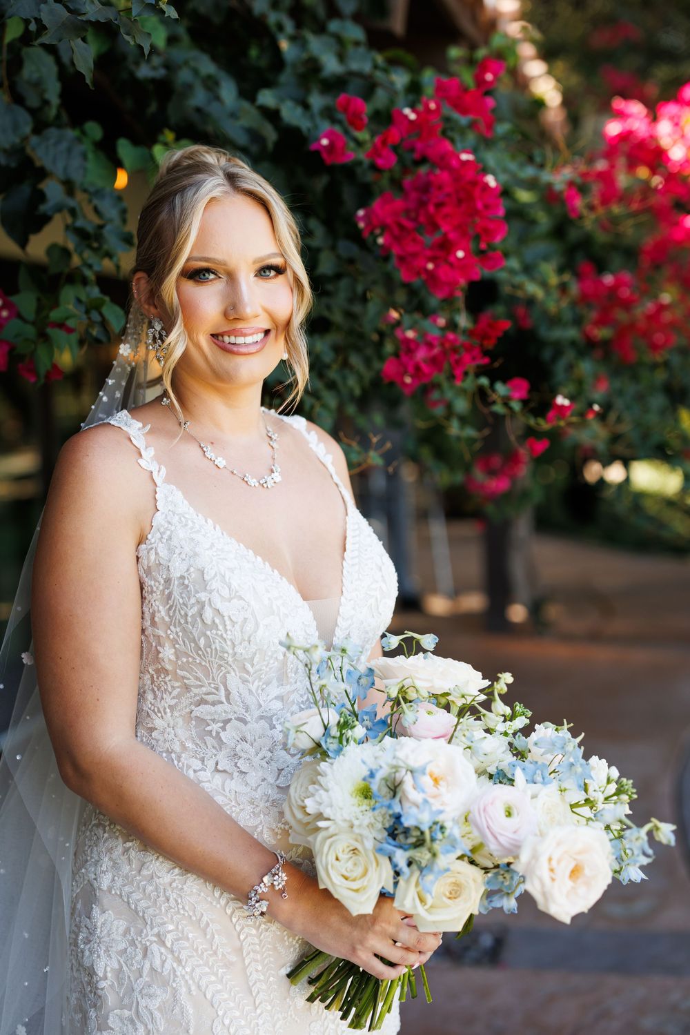 Outdoor bridal portrait with vibrant red bougainvillea flowers and a romantic white lace wedding dress.