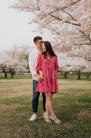 A couple embraces while standing among blooming cherry blossom trees in a park during spring.