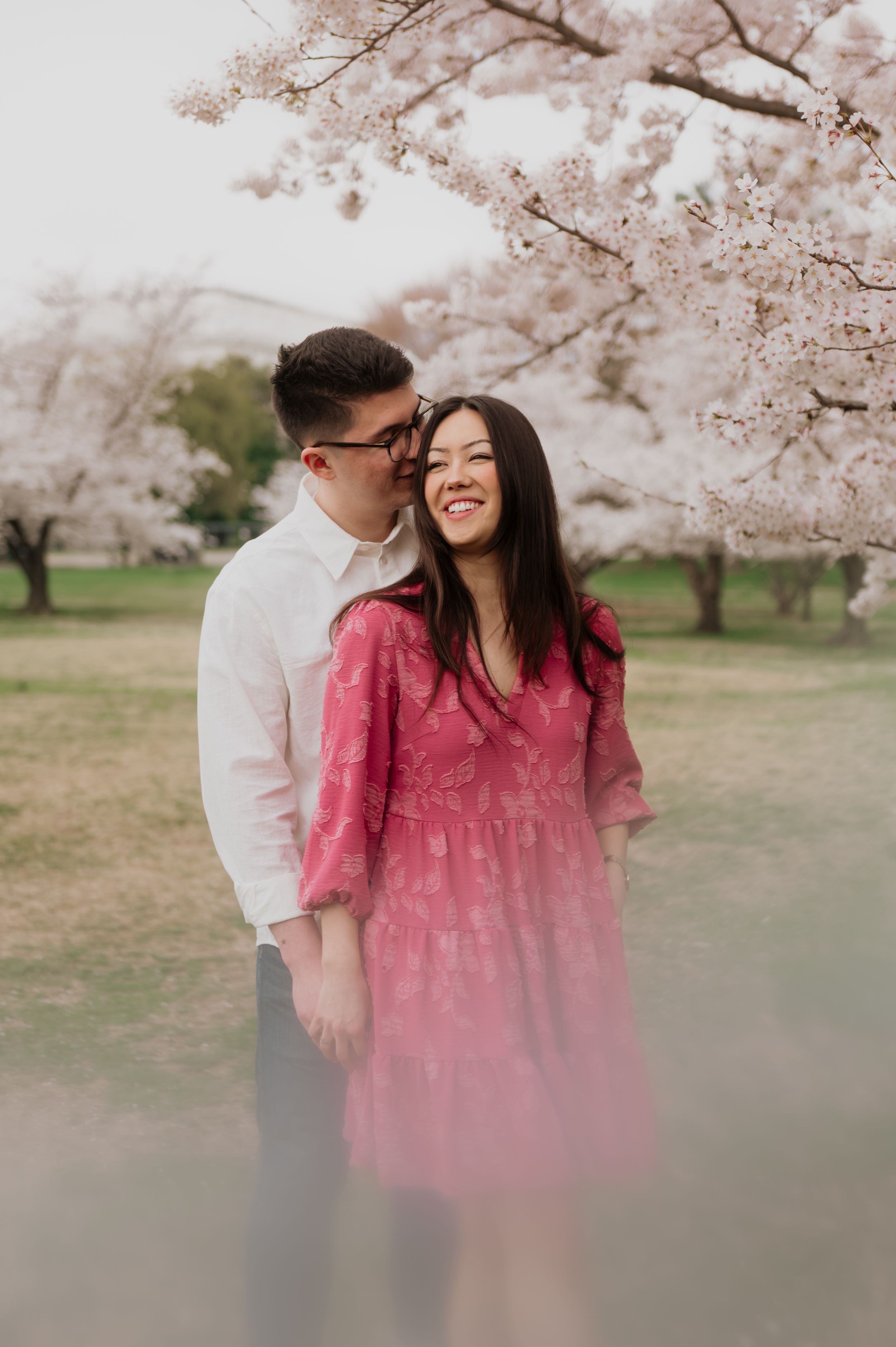 A joyful couple sharing a tender moment beneath blooming cherry blossoms in springtime.