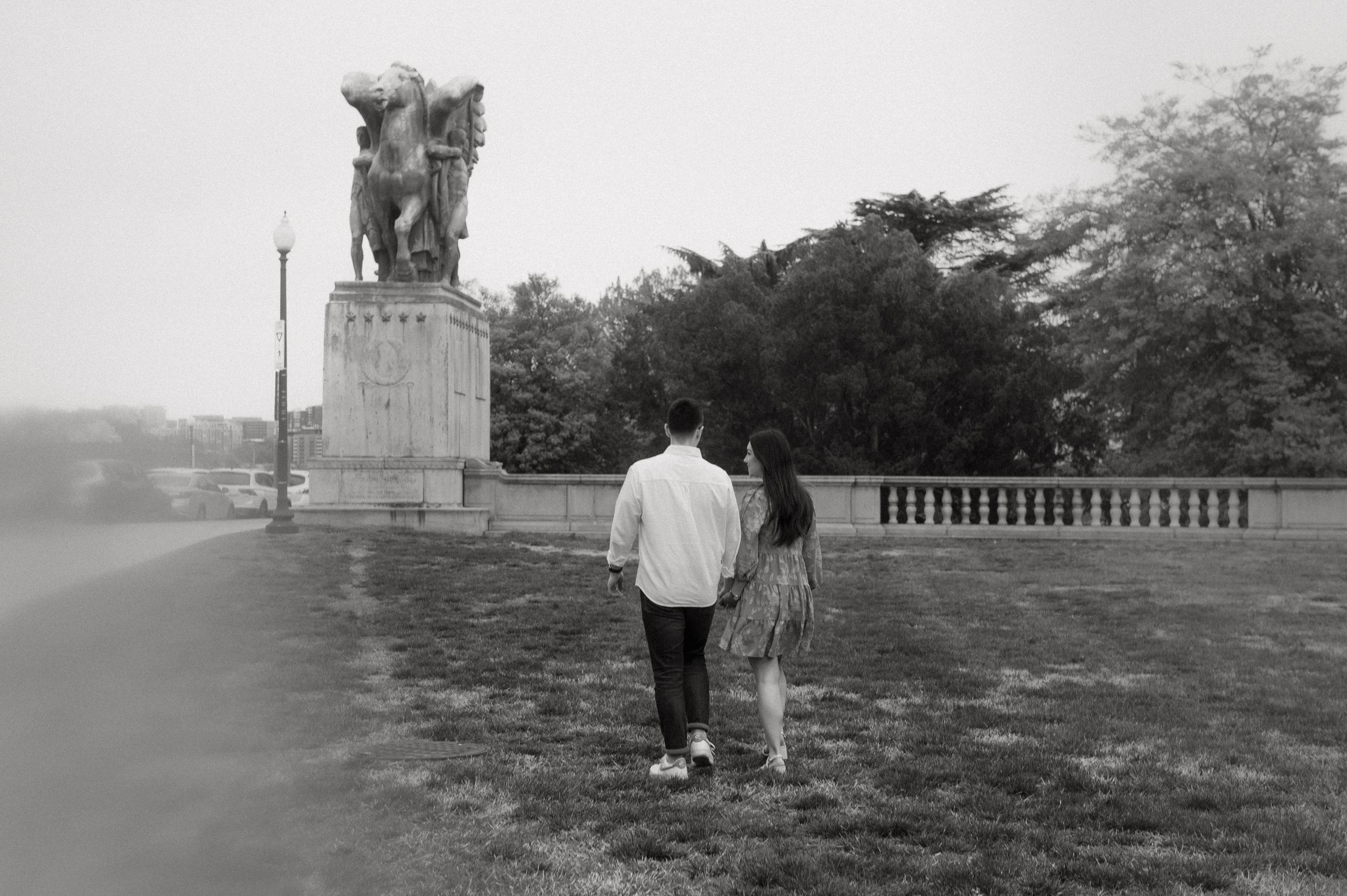 A couple stands together viewing a stone monument at dusk in a black and white photograph.
