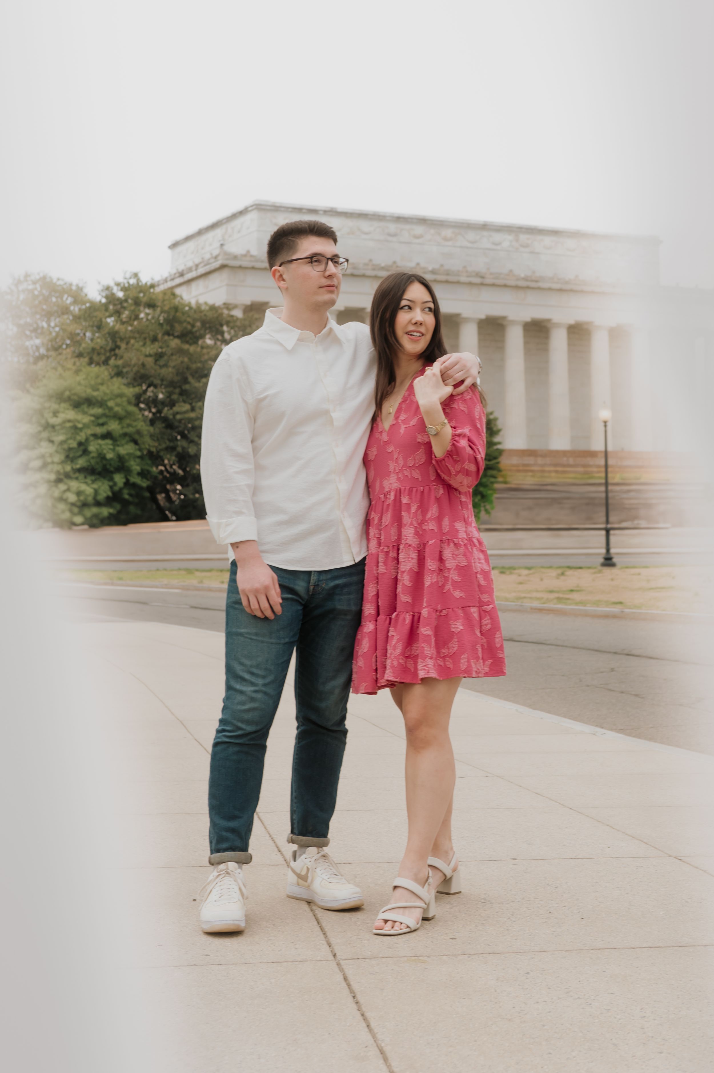 A couple poses together in front of a classical building wearing coordinated pink and white outfits.
