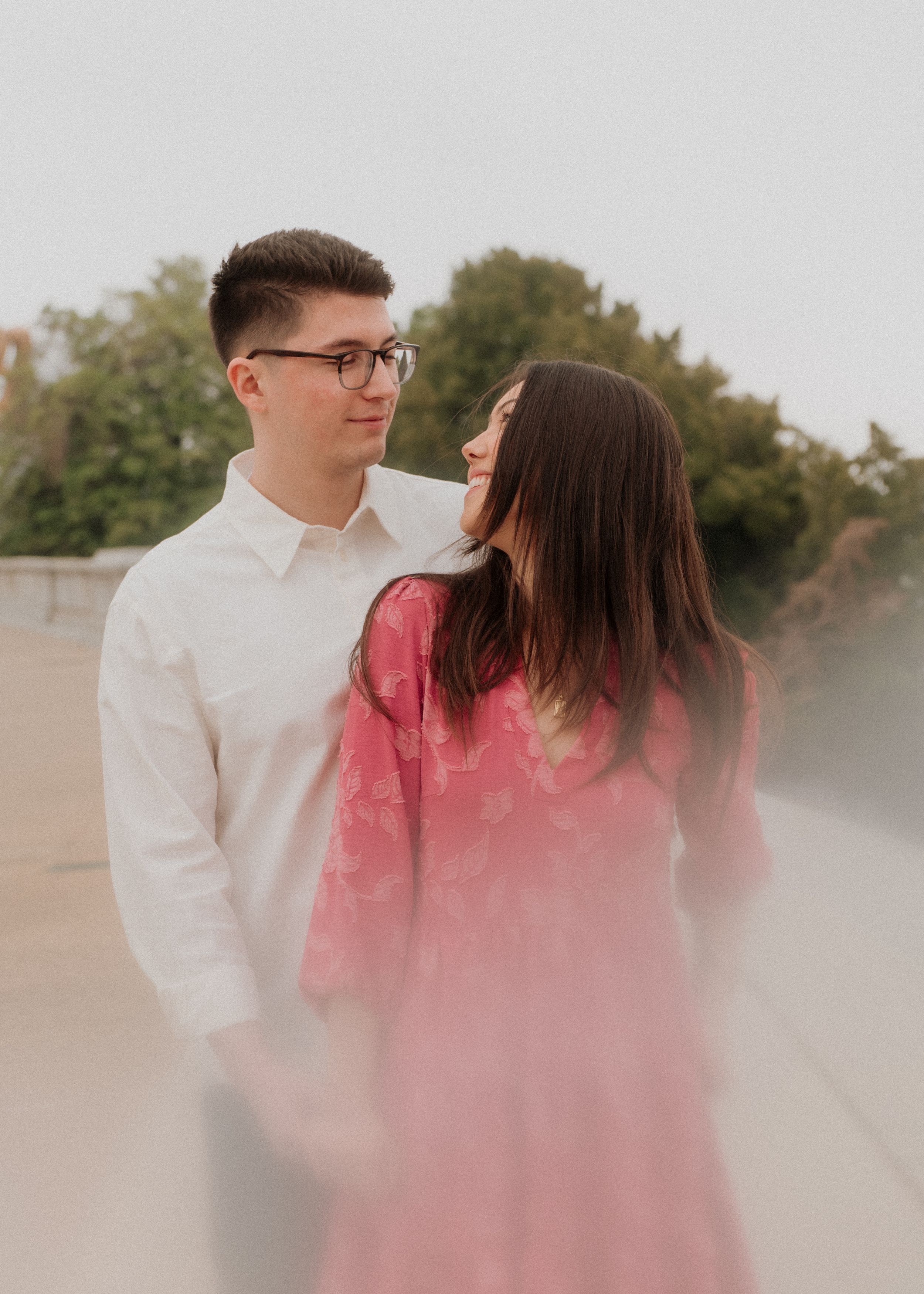 A romantic couple embraces in soft pink fog during a dreamy outdoor photoshoot.
