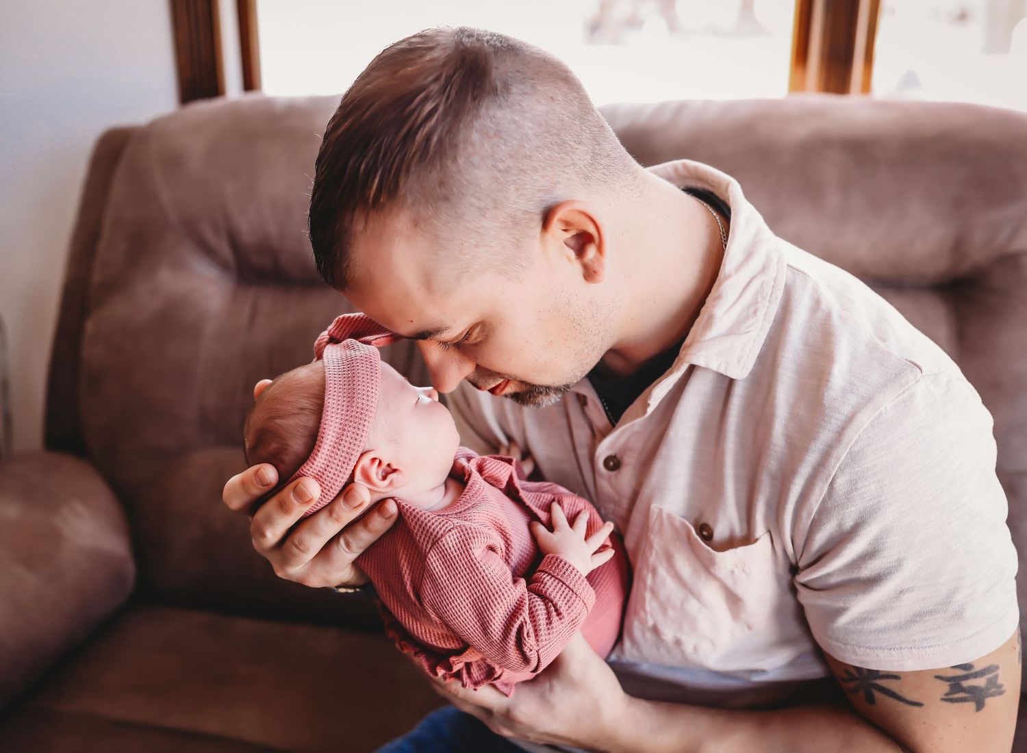 A parent tenderly holds and comforts a crying baby on a brown leather couch in warm lighting.