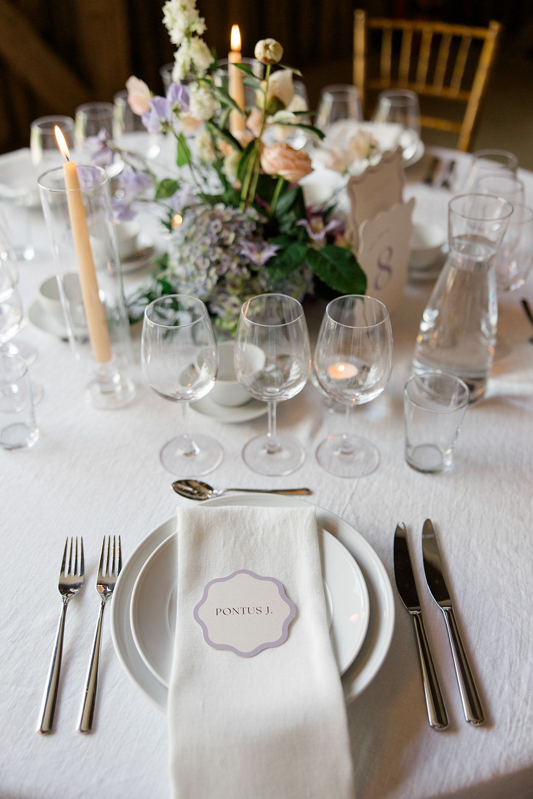 Elegant wedding reception table setting with white linens, crystal glassware, and soft floral centerpieces.
