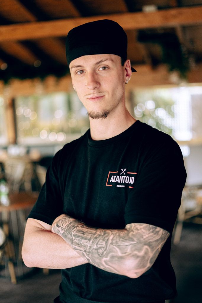 Retrato profesional de cocinero con tatuajes con uniforme en interior de restaurante