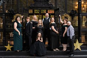 A family dressed in elegant attire standing "Kardashian" style on a porch of a black and gold greenhouse that is decorated for Christmas