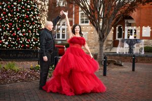 a couple in a suit and red dress dancing in a downtown area that is decorated with a large Christmas tree.