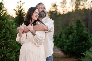 A couple embracing each other looking off into the distance in a Christmas tree farm.