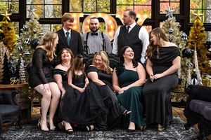 A large family sitting and standing on and around a couch in a black and gold greenhouse that is decorated for Christmas