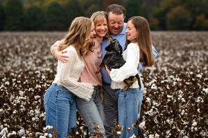 A family of 4 and their dog standing in a cotton field laughing together