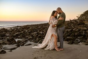 A couple forehead to forehead standing on a rocky beach during sunrise