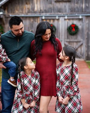 Two parents looking down at their two daughters in front of a brown wooden barn on a brick path