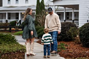 a family of 3 walking together down a path towards a historic white house
