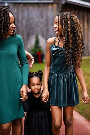 a mom and her two daughters wearing green standing in front of a wooden barn.