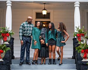 A family of 5 standing on porch steps that are decorated for the Christmas holiday