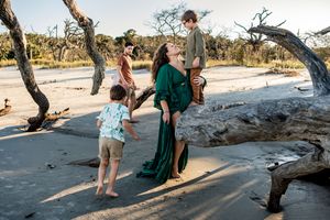 A mom and her sons standing on a beach on large driftwood trees that have fallen