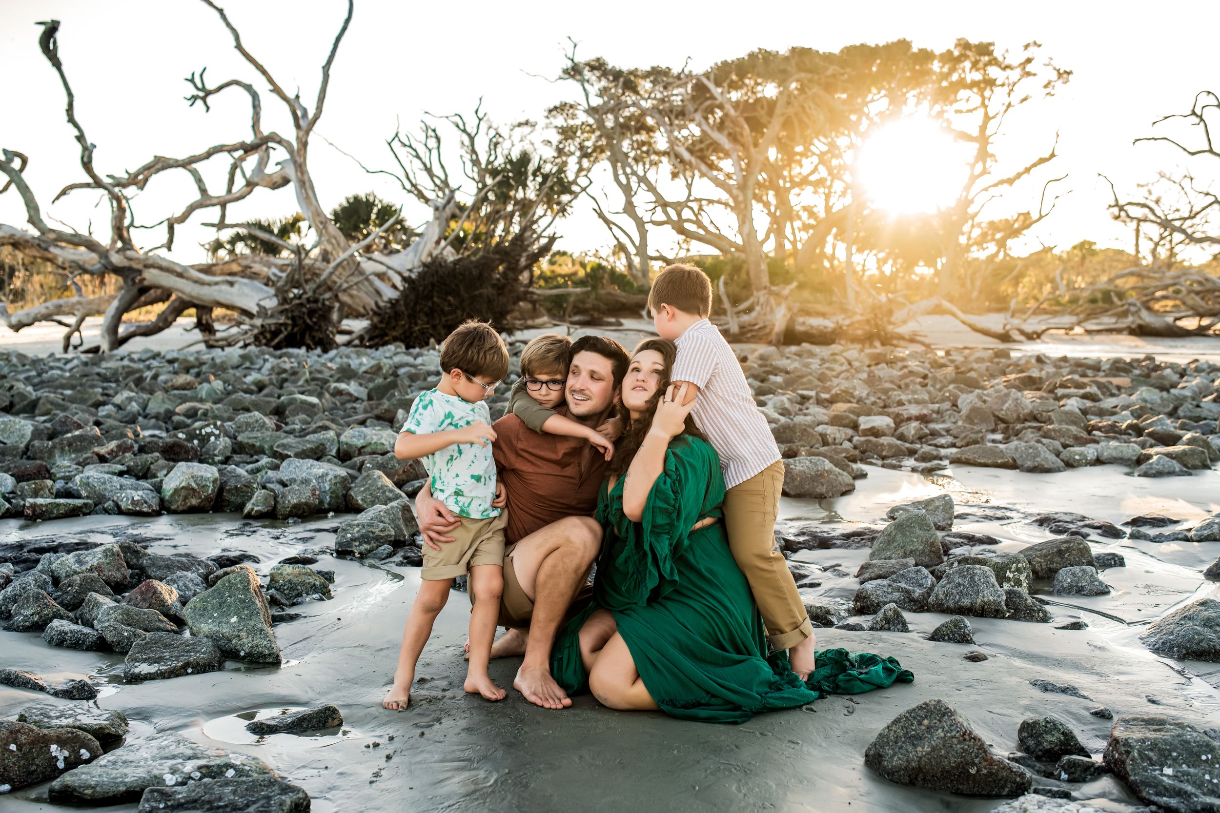 A family playing together on a rocky beach during sunset