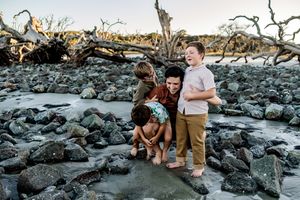 a dad and his sons playing on a rocky beach during sunset