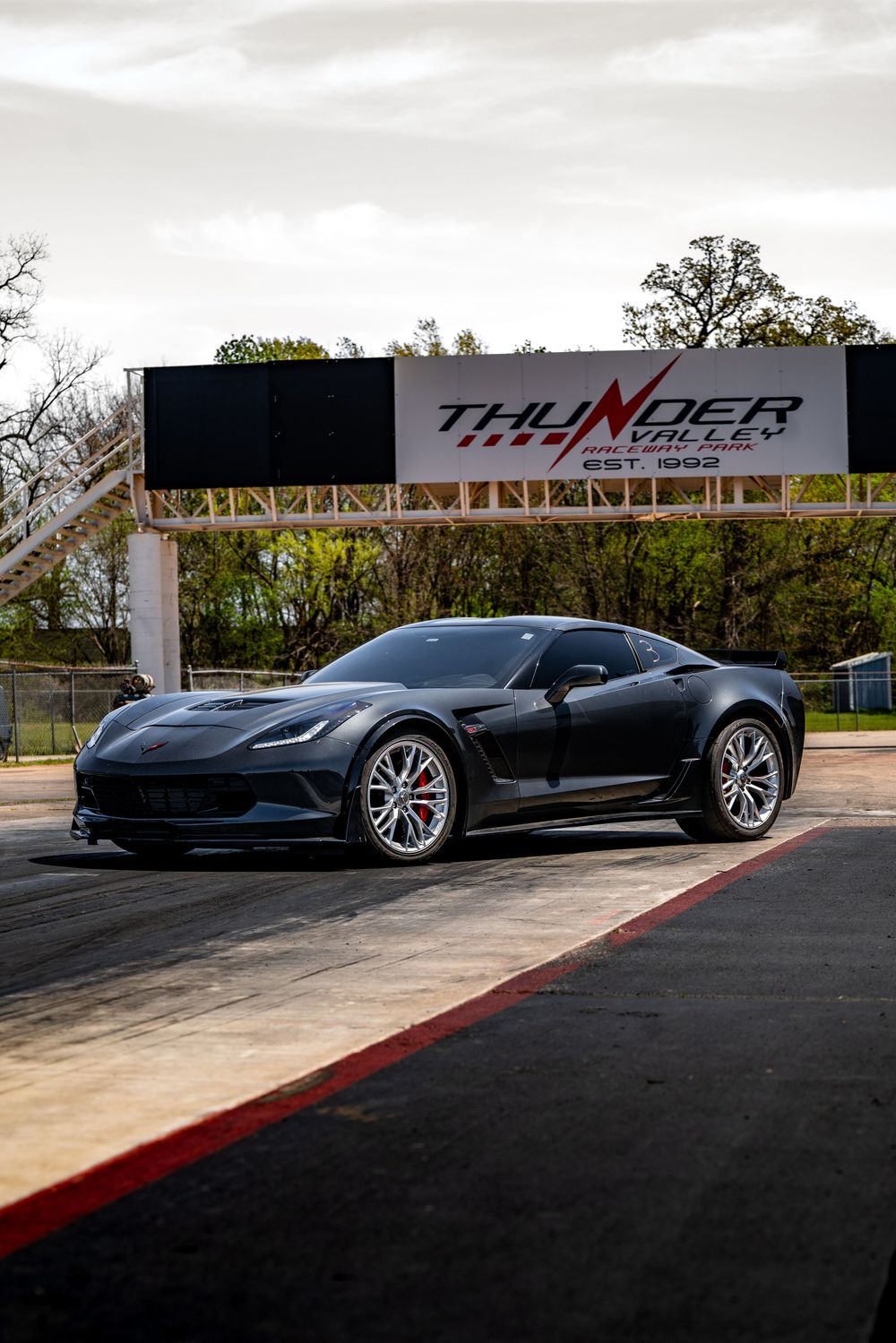 Black Chevrolet Corvette Z06 parked on a racetrack with Thunder Motorsports signage in the background.
