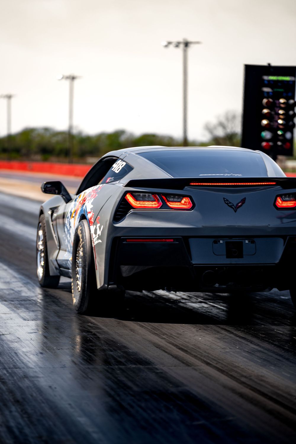 Black Chevrolet Corvette rear view on drag strip showing distinctive taillights and aggressive stance.