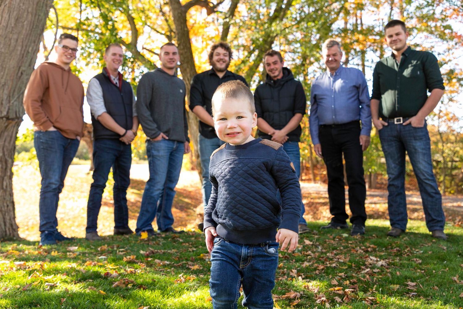 A group of men all standing in a line slightly blurred, with a young child standing close to the camera in focus