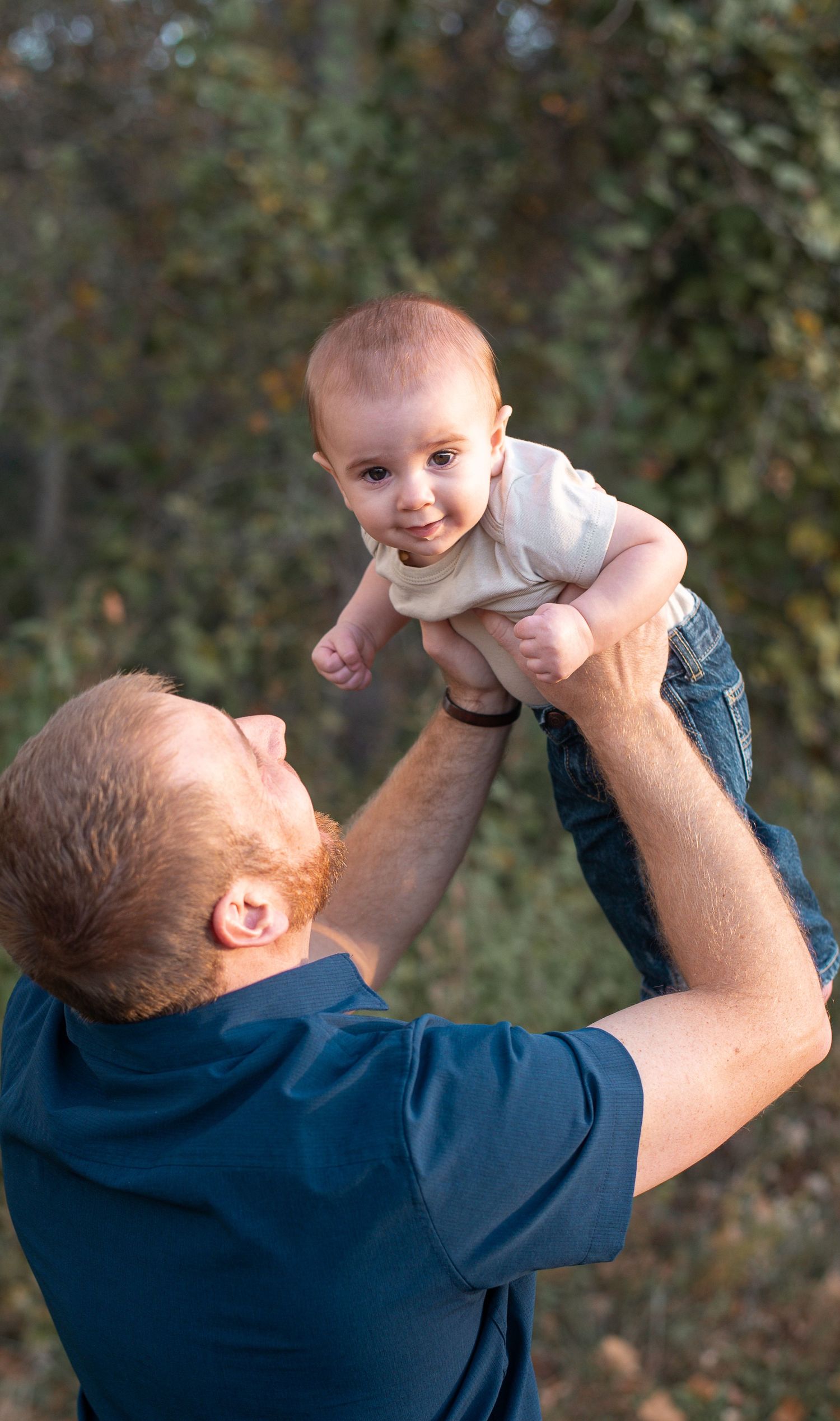 A dad holding his kid in the air while the kid looks at the camera. Family photography