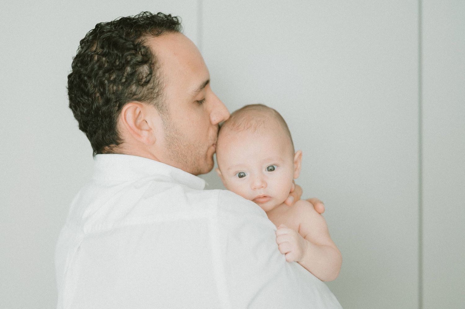 Tender moment between parent and baby in white against light background.