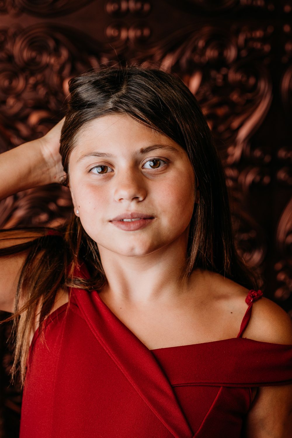 Portrait of a youth in a red off-shoulder top against an ornate dark backdrop.