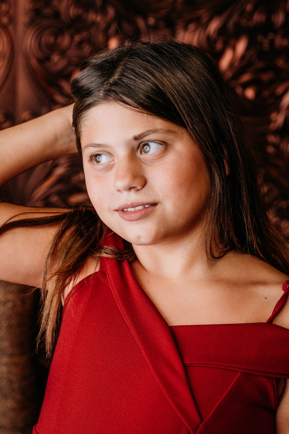 Portrait shot with coppery tones featuring dark hair against a textured brown backdrop wearing a red sleeveless top.