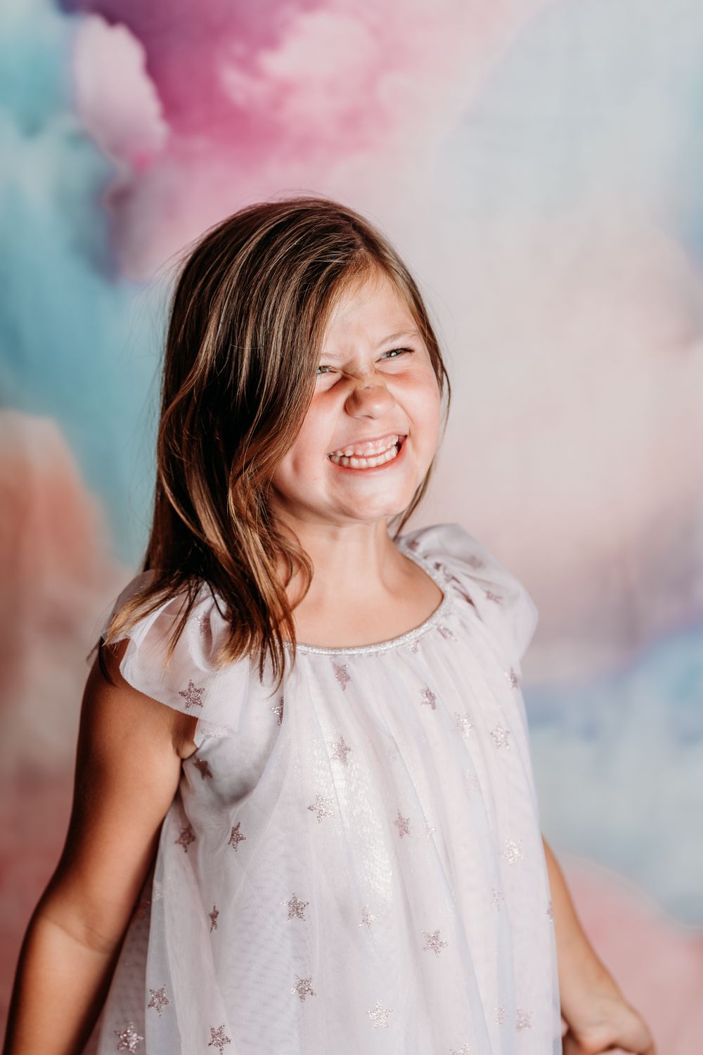 Portrait with colorful cotton candy clouds background showing genuine joy and laughter in white dress.