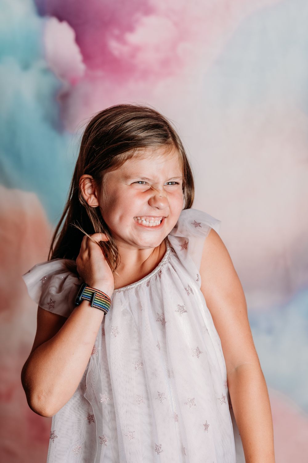 A person in white lace smiles and laughs joyfully against a pink and blue cotton candy colored background.
