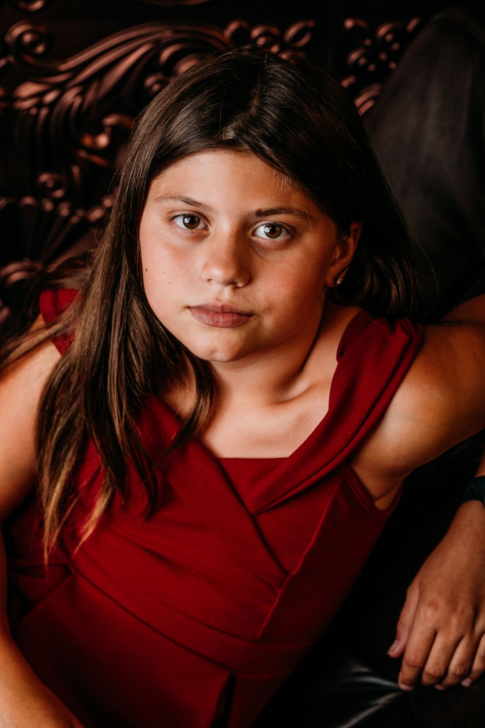 Portrait photo of a child wearing a red sleeveless top against a dark background.