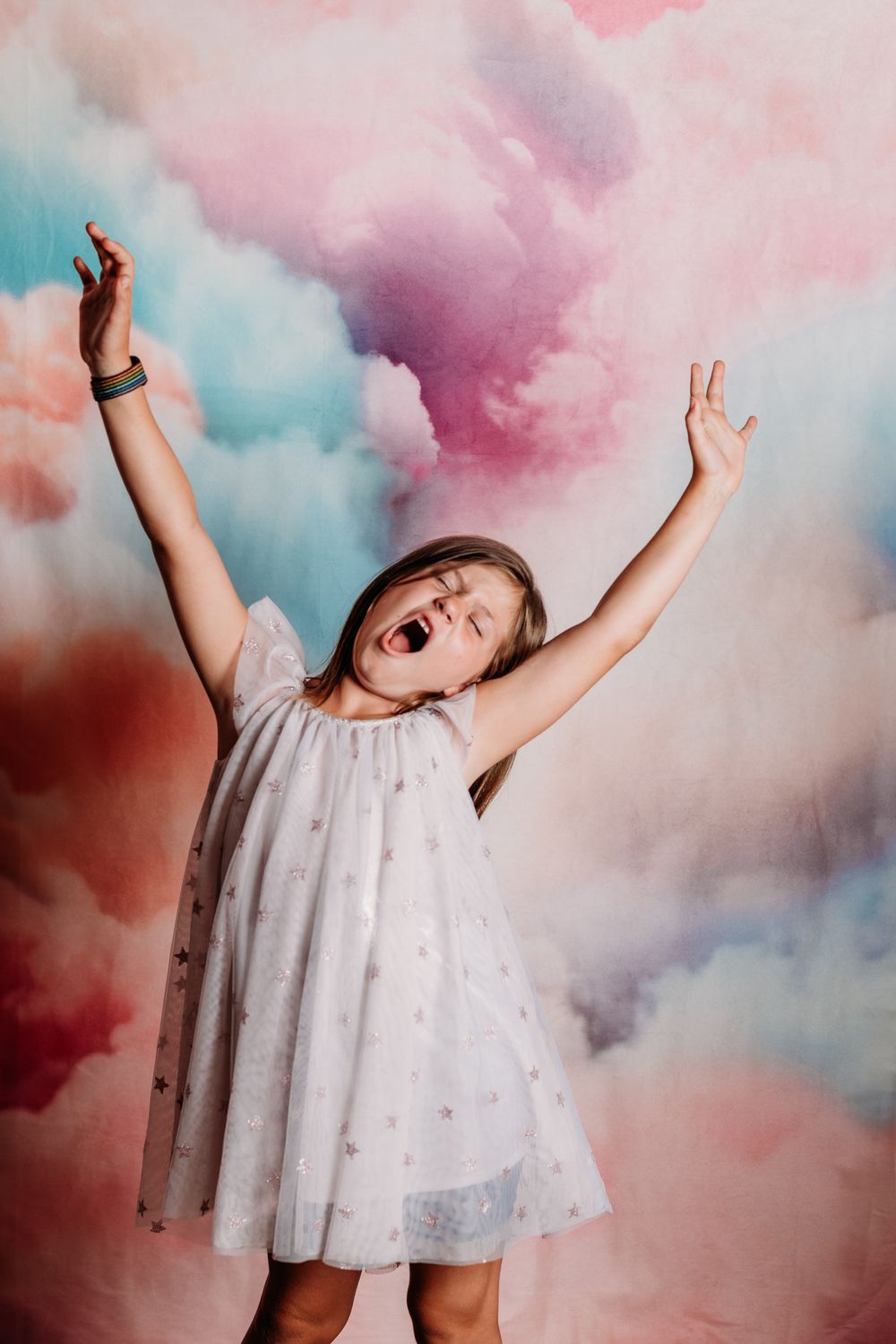 A person in a white tulle dress dances joyfully against a dreamy pink and blue smoke background.