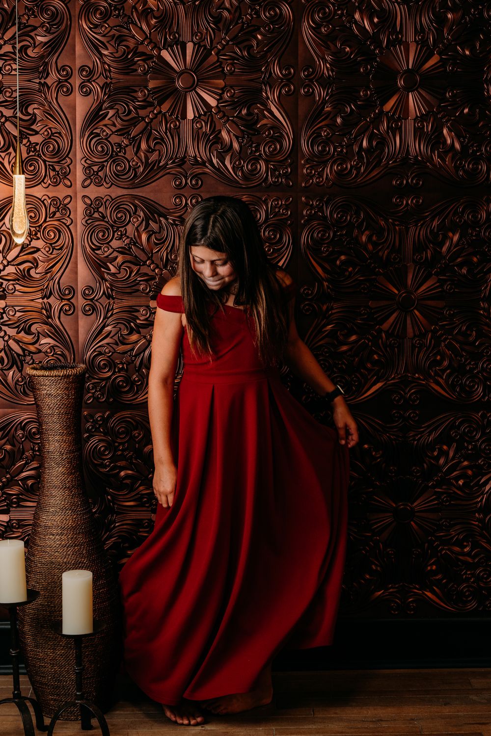 Dramatic series of a woman in a flowing red dress posing against an ornate brown wall with decorative candles.