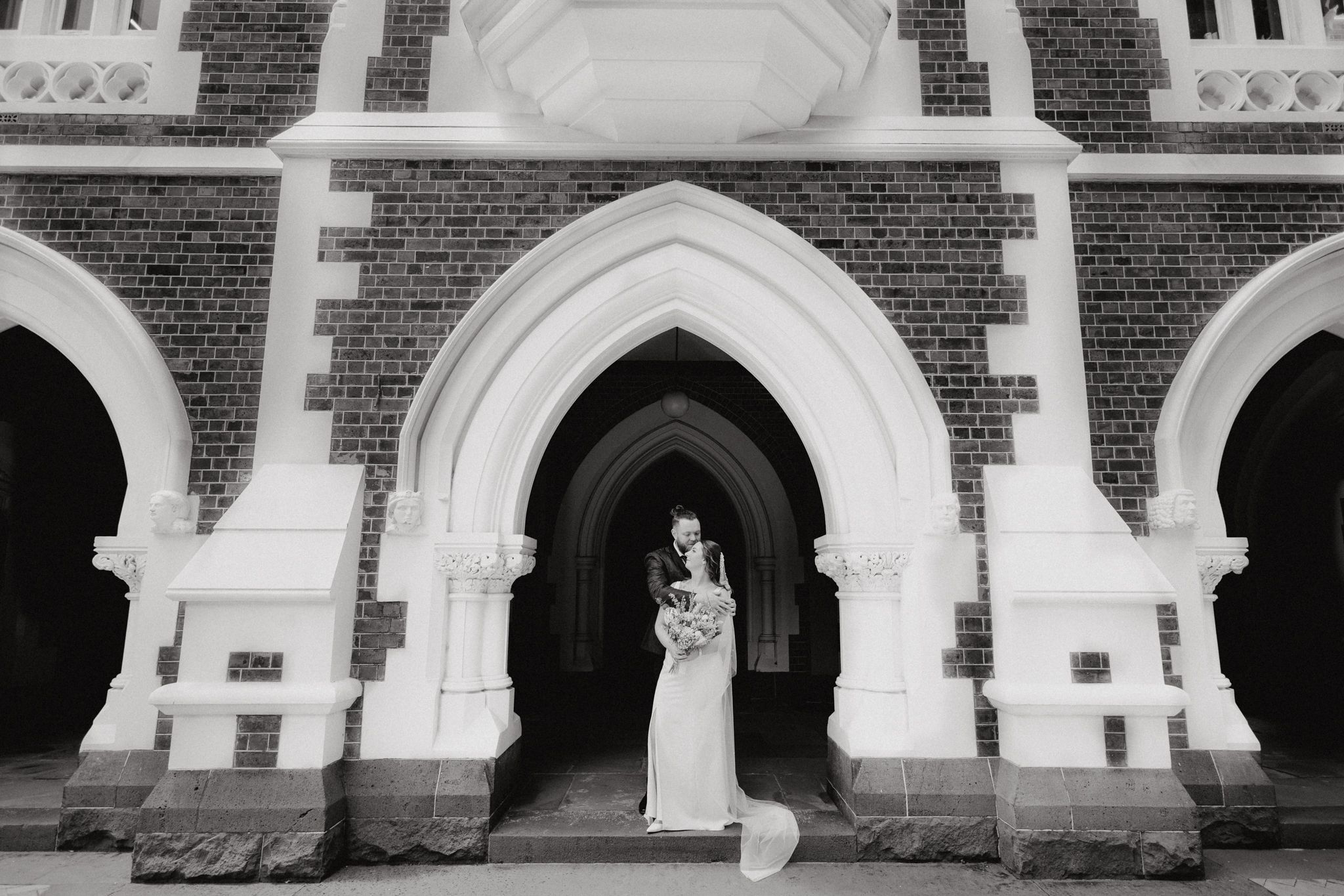 Classic black and white wedding photo of bride standing in archway, captured by Apertured Media Auckland Wedding Photographer.
