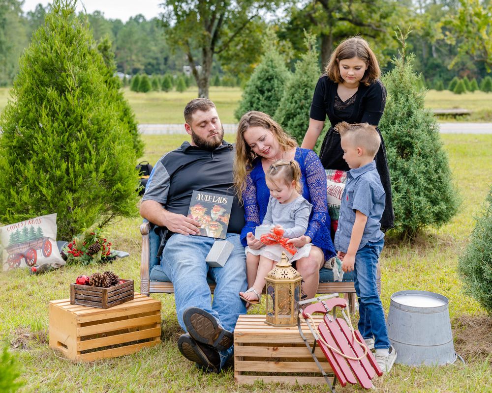 Family gathering at Christmas tree farm with wooden crates and holiday decorations among evergreens.