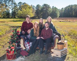 Family holiday portrait on brown couch with decorated Christmas tree in outdoor field setting.