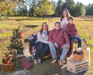 Casual family portrait on brown couch with Christmas decorations in outdoor field setting.