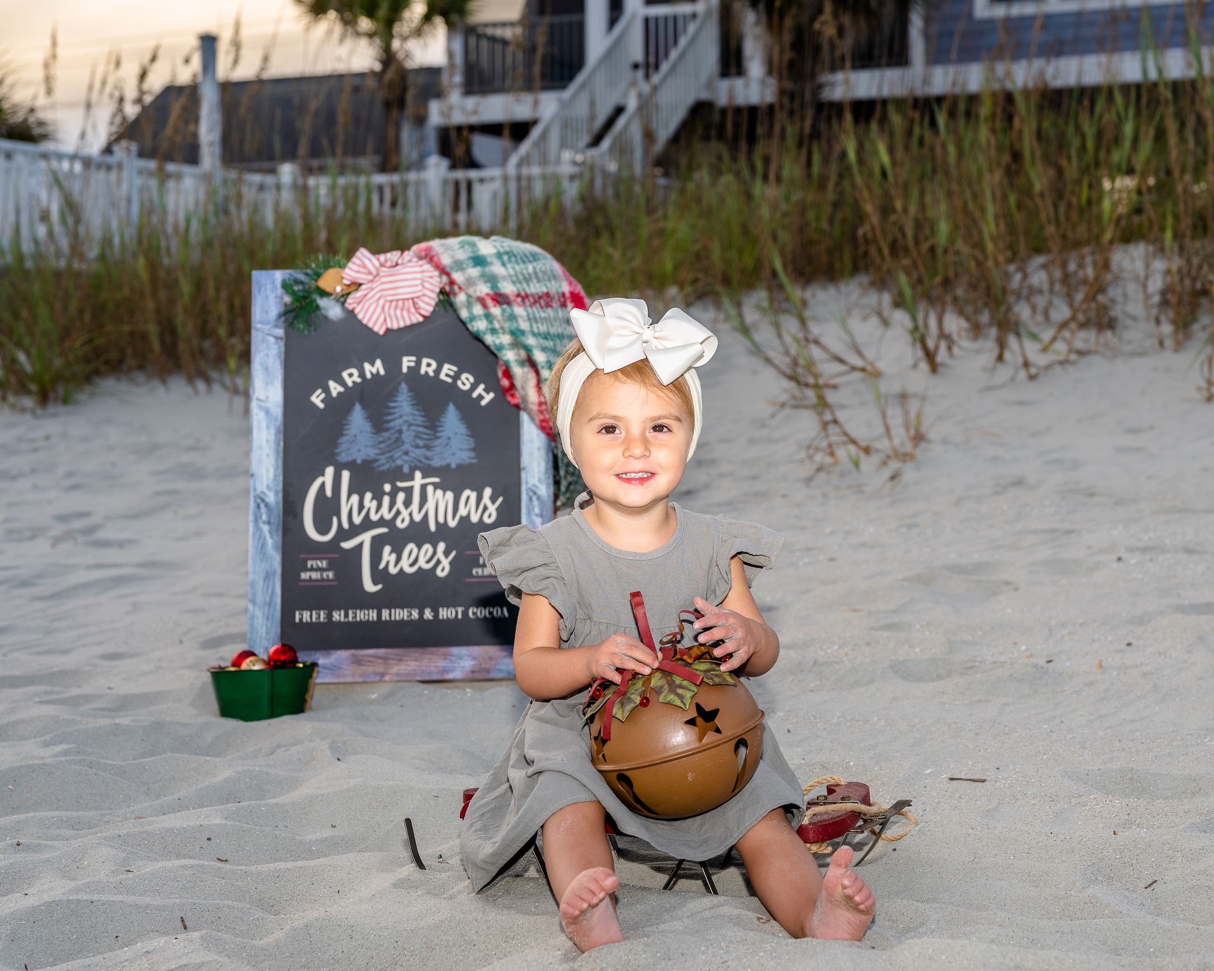 Beach holiday photo setup with child sitting next to Christmas book and decorations on sand.