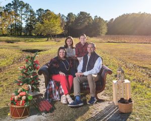 Outdoor family photo session with small Christmas tree and rustic decor at golden hour.