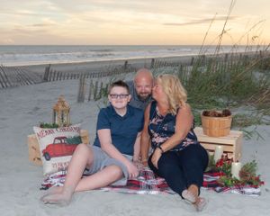 Beach sunset scene with group sitting on blanket surrounded by holiday decorations and sand fences.
