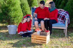 Family group relaxes on outdoor furniture among Christmas trees with wooden crate decorations.