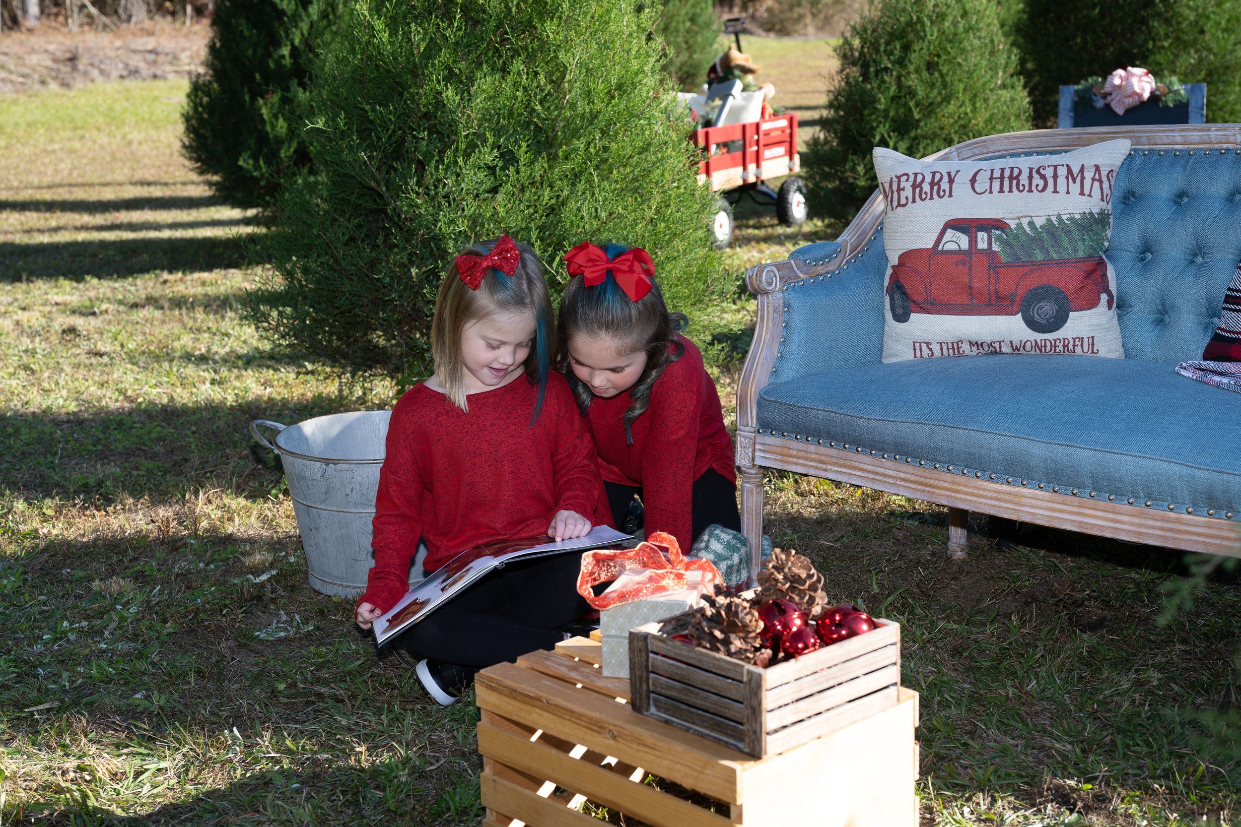 Two figures in matching red outfits sit on wooden crates examining holiday decorations outdoors.