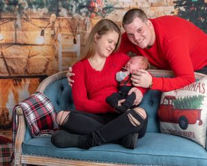 Indoor holiday scene with couple on blue sofa surrounded by Christmas pillows and decor.