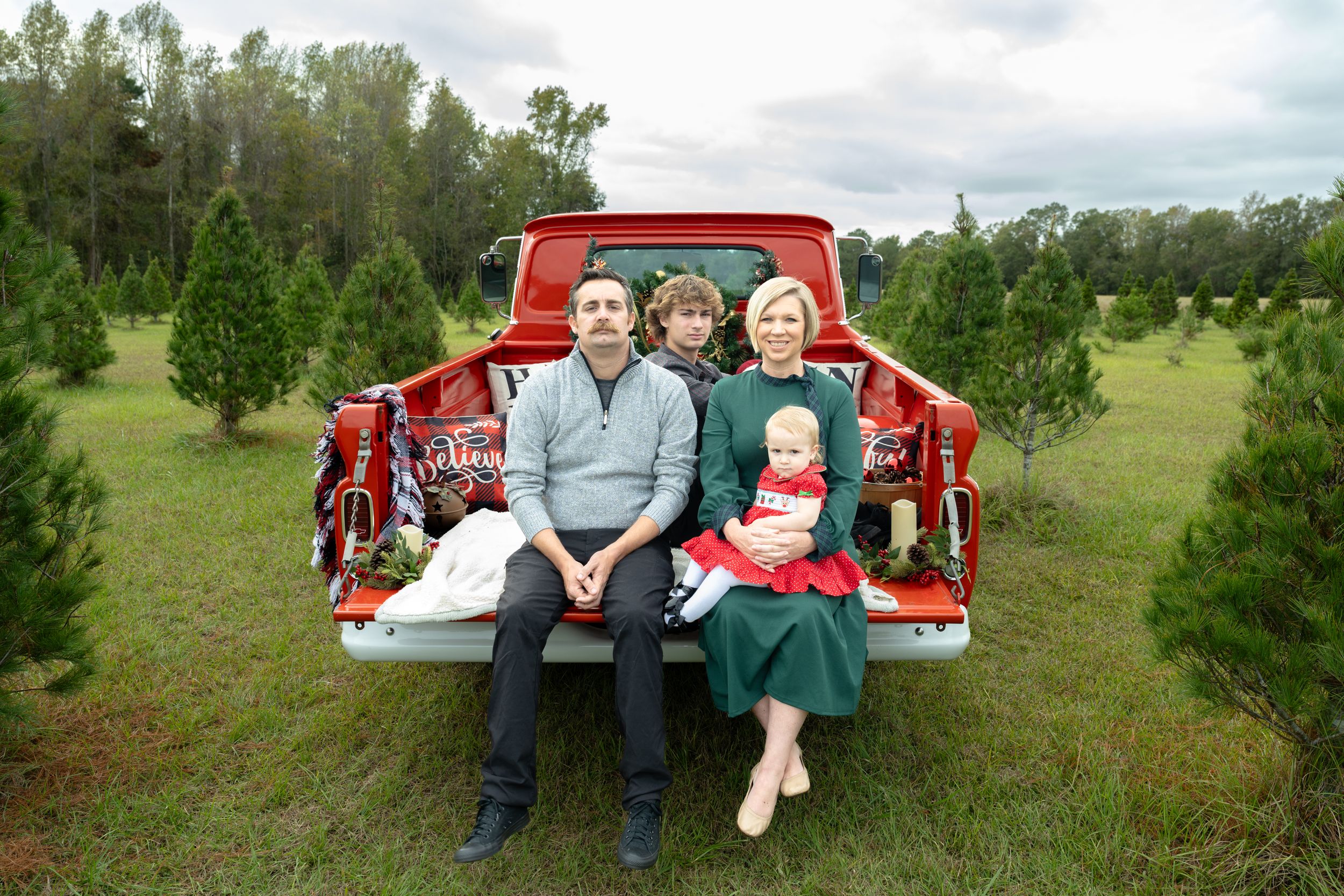Family holiday portrait in the back of a vintage red pickup truck at a Christmas tree farm.