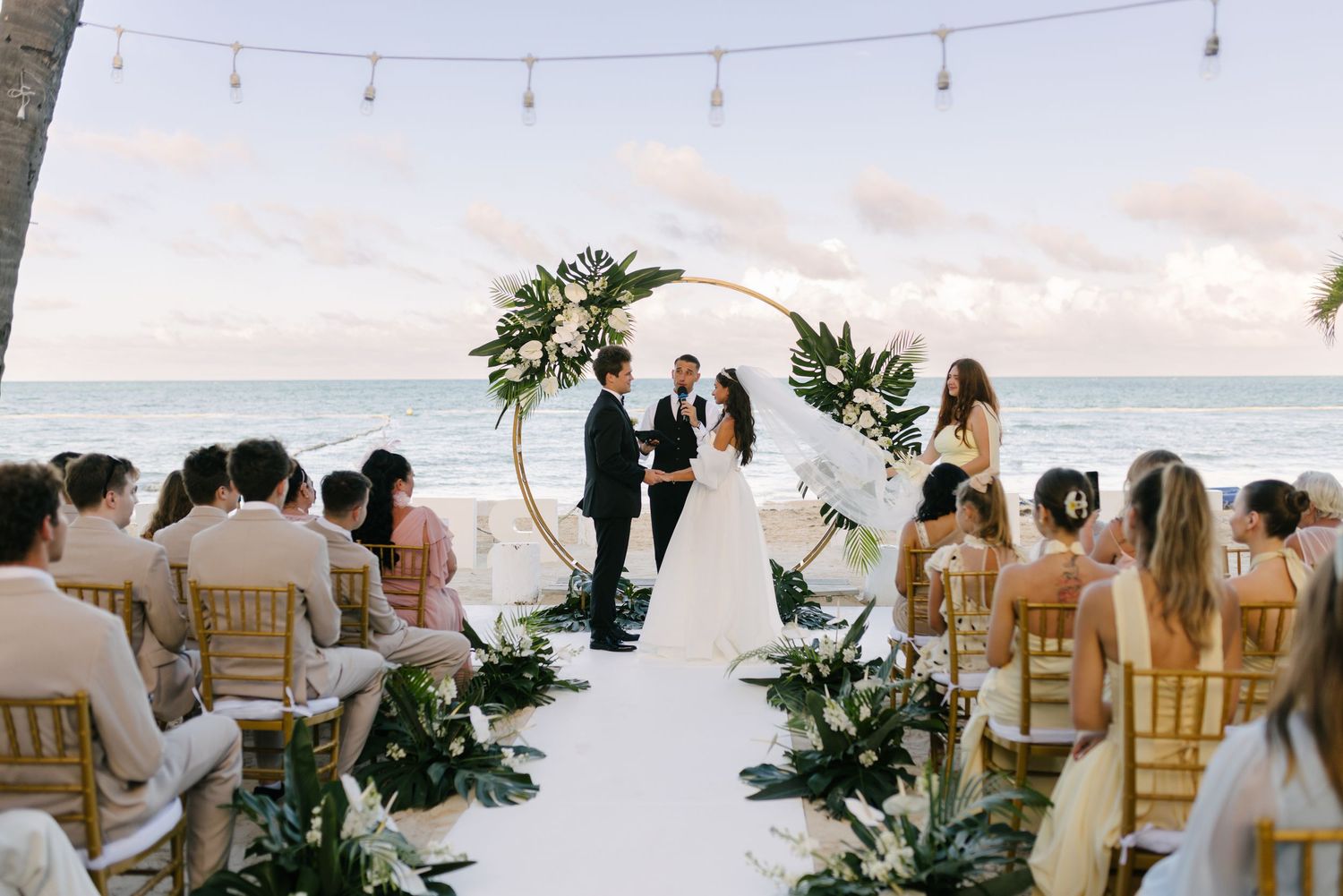Guests seated for a lakeside ceremony beneath a greenery arch.