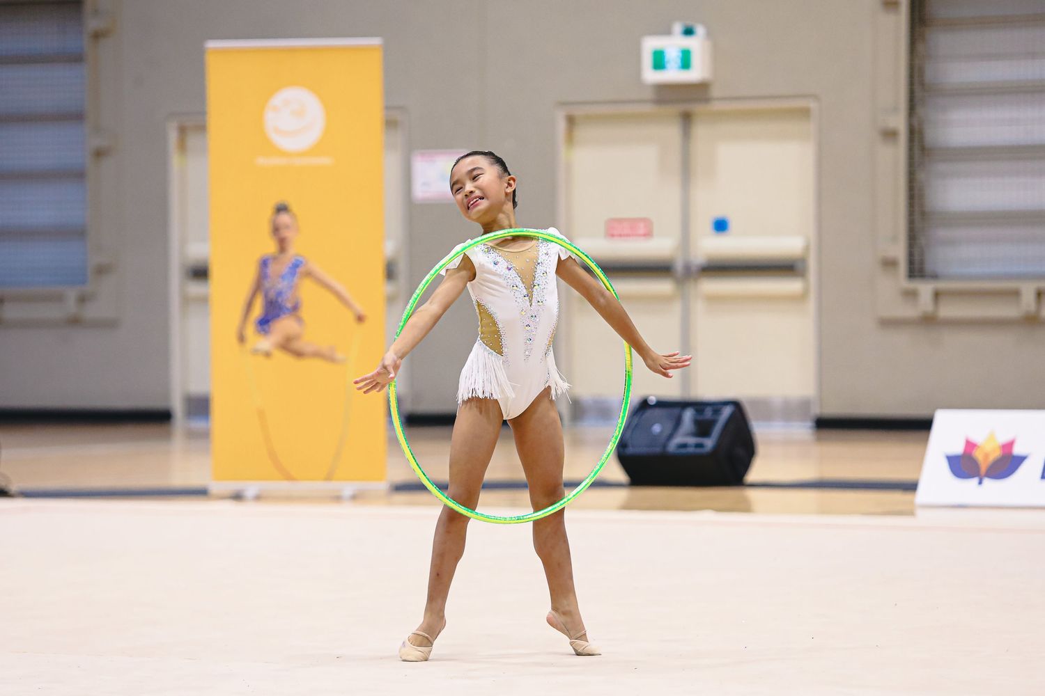 Rhythmic gymnast performs graceful routine with ribbon against pink backdrop during competition.