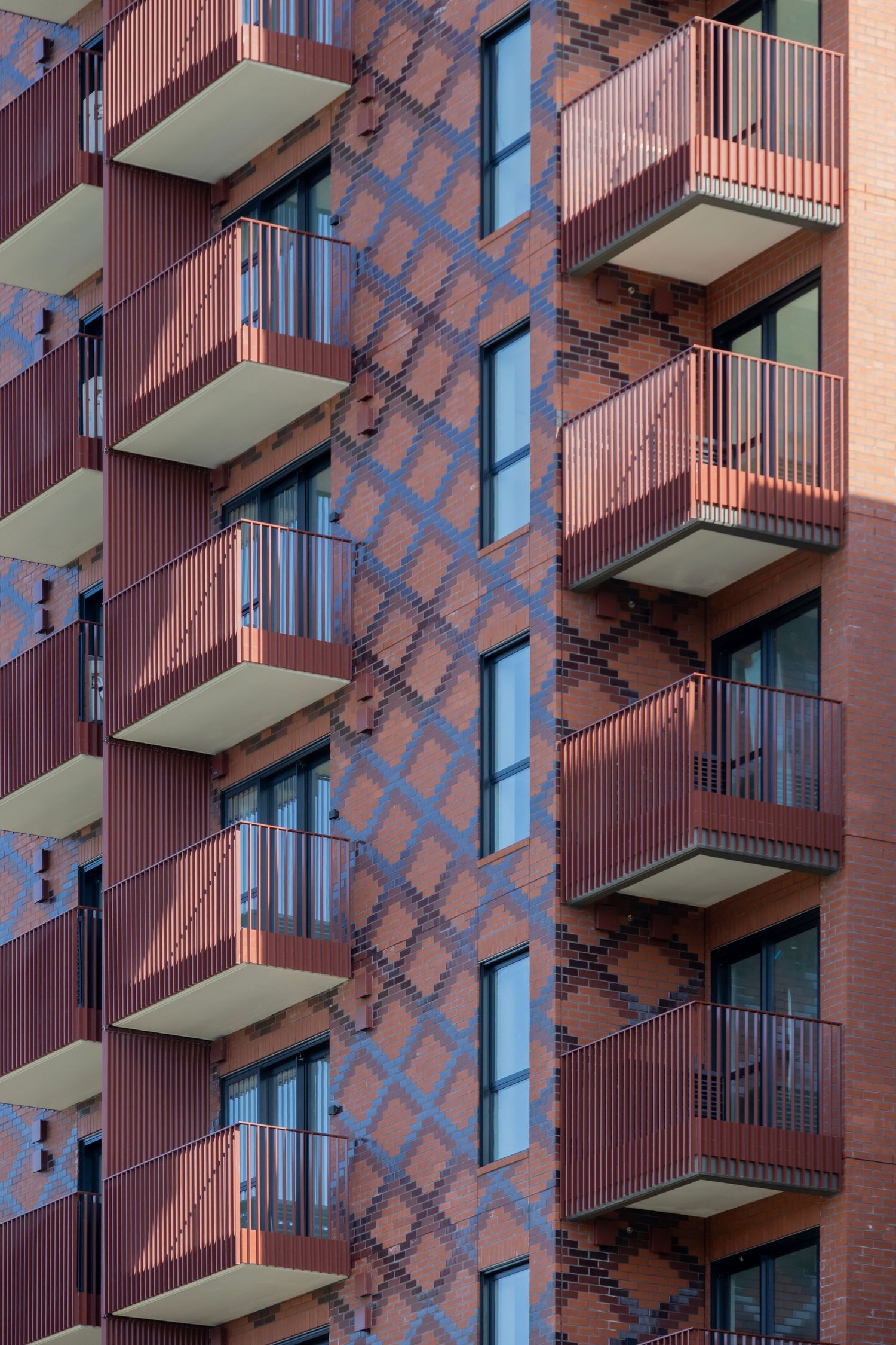 Patterned brick facade punctuated with protruding red balconies on each level.